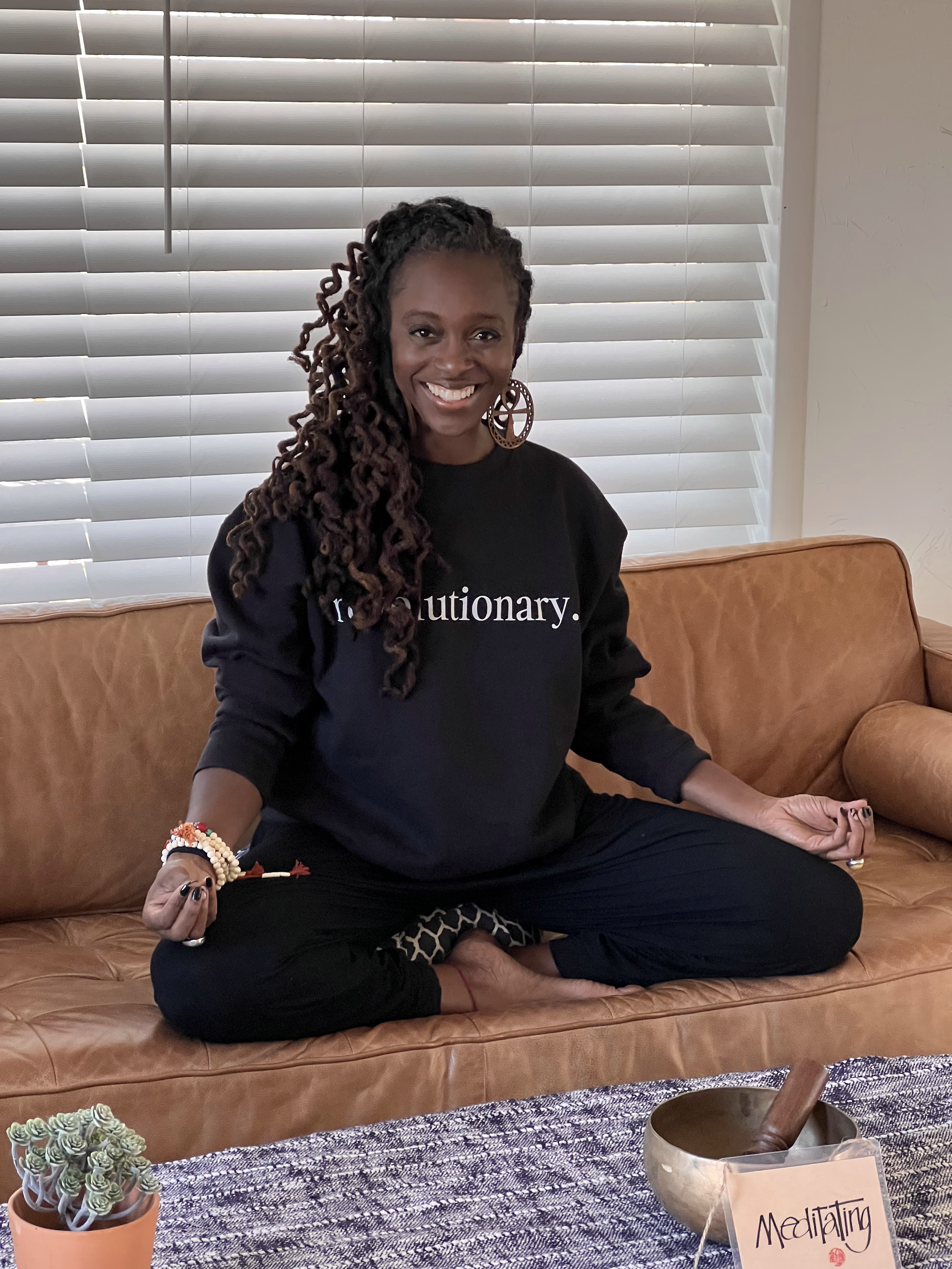 jylani ma'at seated cross-legged, smiling, wearing a sweatshirt that reads revolutionary