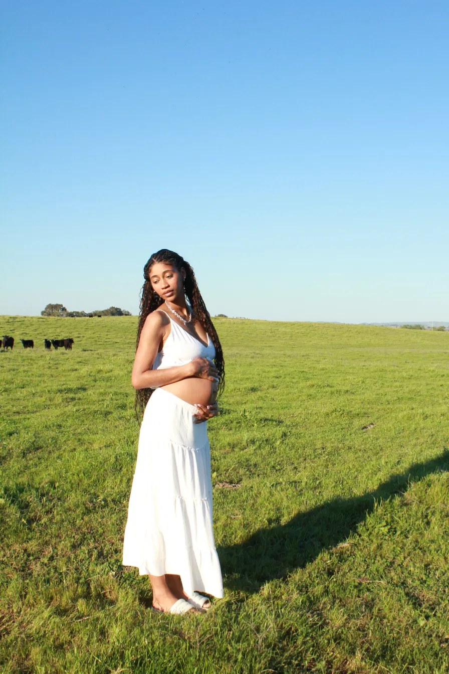 Pregnant woman standing in a green field, hand resting on her belly